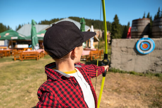 Portrait boy holding bow shooting target mountain field. Sunny summer day forest hills scenery. Outdoor games kids. Archery training summer camp. Active childhood development travel leisure hobby conc