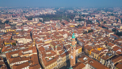Obraz premium Aerial view of Vicenza, Italy, showcasing its historic city center, terracotta rooftops, and the iconic Torre Bissara under a hazy winter sky.