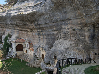 Obraz premium San Bernabé Hermitage in Ojo Guareña - Historic Hermitage of San Bernabé built into the massive limestone rock face and cave entrance of the Ojo Guareña complex in Burgos, Spain.