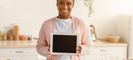 A woman stands in a bright kitchen holding a tablet. She is smiling as she prepares ingredients for a cooking session. The kitchen has various food items and utensils on the counter. © Prostock-studio