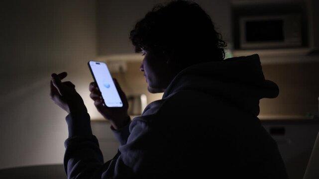 Young student studying at night in dark apartment using smartphone and laptop communicating with chatgpt asking questions ai assistant helping with lessons and homework