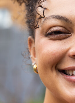 African American woman smiling and squinting outdoors, showing gold hoop earring, teeth showing