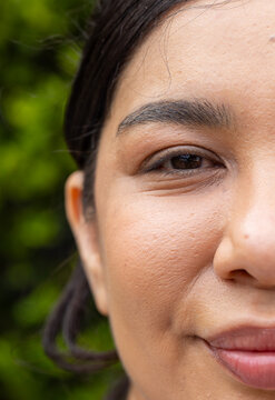 Woman looking toward camera, showing closeup right-side face at outdoor green foliage