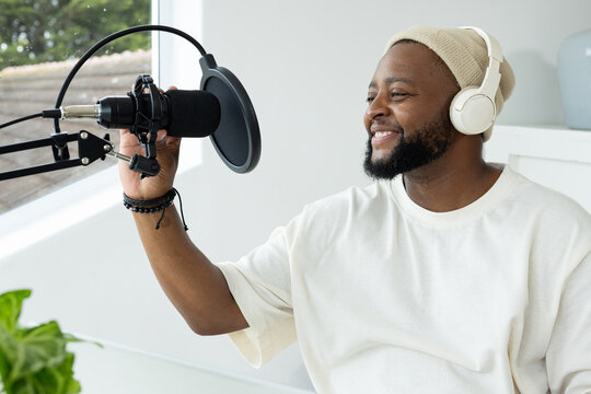 African American man sitting in studio next to window recording podcast with microphone, headphones