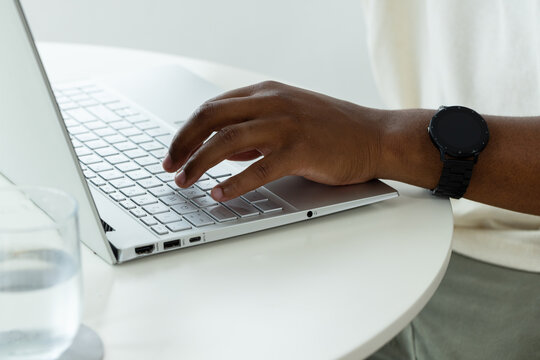 African American man typing on laptop at table in light shirt, black wristwatch, water glass nearby