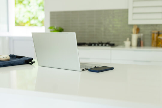 Silver laptop sitting partially open on island, smartphone and sleeve resting, gas stovetop visible