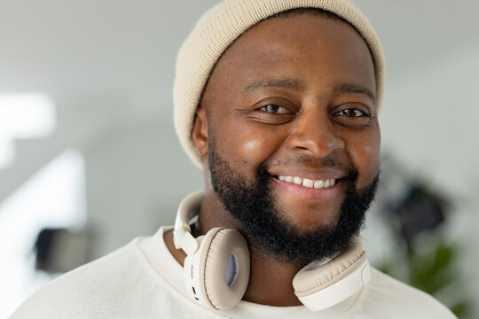 African man smiling while wearing cream knit beanie and beige headphones at studio corner