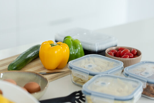 Yellow bell pepper is sitting on wooden cutting board on kitchen counter with meal prep containers