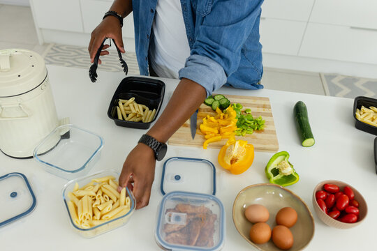 Adult African American man arranging penne into glass containers on white counter with black trays