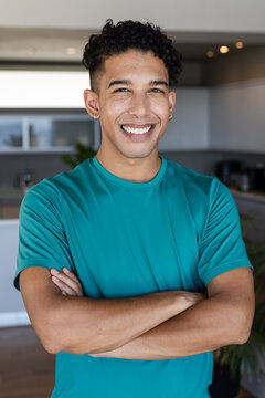 Adult African American man standing with arms crossed in kitchen wearing teal shirt, hoop earrings