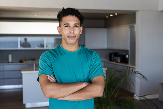 Adult African American man standing by kitchen island wearing teal t-shirt and hoop earrings