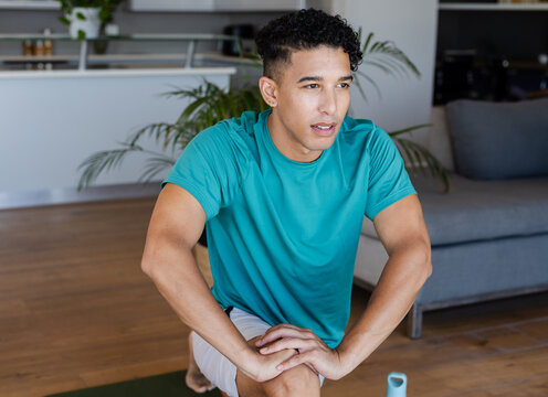 African American man performing lunge on green mat at home wearing teal tee, water bottle nearby