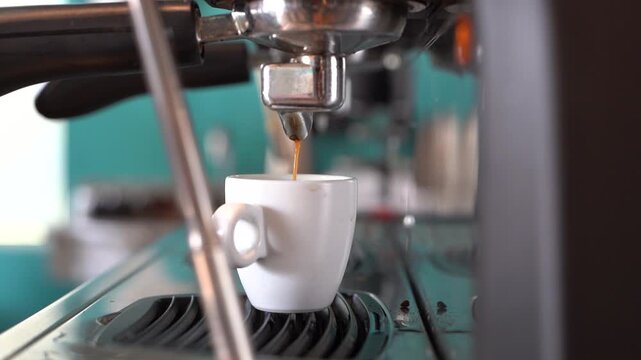 A coffee machine is dispensing hot coffee into a white cup. The coffee is freshly brewed and the cup is clean and empty. The coffee machine is located in a kitchen