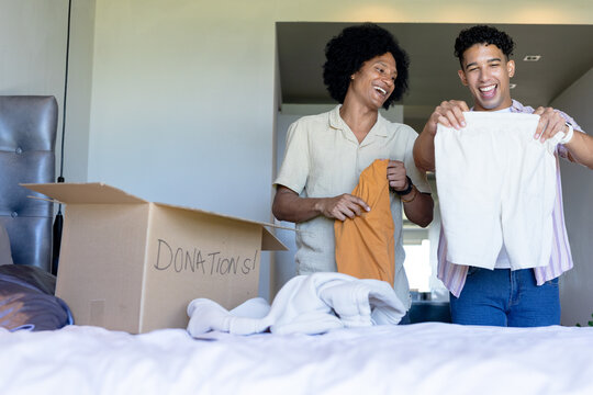 Two African American men standing by bed sorting clothing into cardboard box labeled DONATIONS