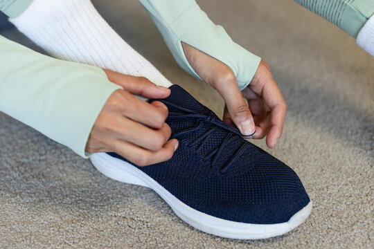 African American woman fastening navy laces on beige carpet, wearing green thumbhole top or white so