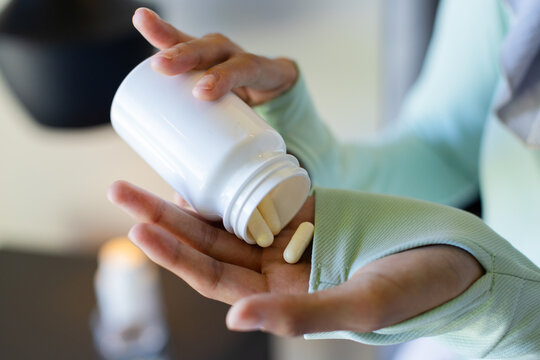 African American woman in mint thumbhole top pouring capsules from pill bottle into palm at counter