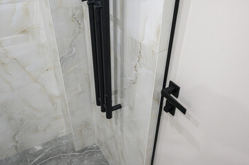 Obraz premium Modern bathroom corner with marble-effect tiles, matte black heated towel rail, sleek white door with black handle, grey marble floor — minimalist design