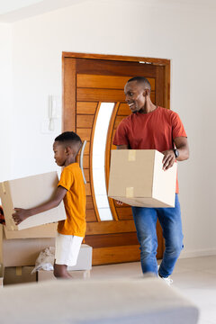 African father and youth son carrying sealed cardboard moving boxes in foyer at door intercom