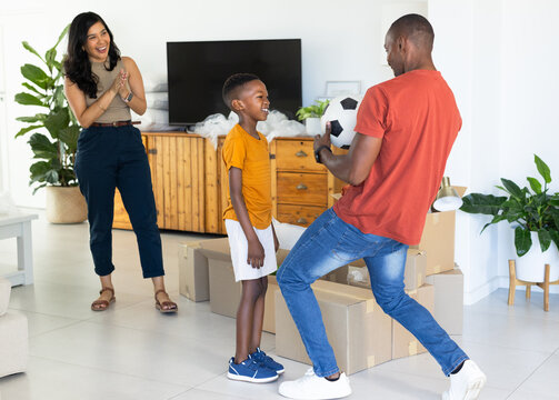 Diverse family playing with soccer ball, unpacking boxes and laughing in modern living room