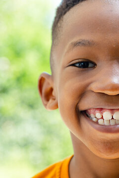 African child boy smiling and showing teeth, looking at camera in garden wearing orange T-shirt