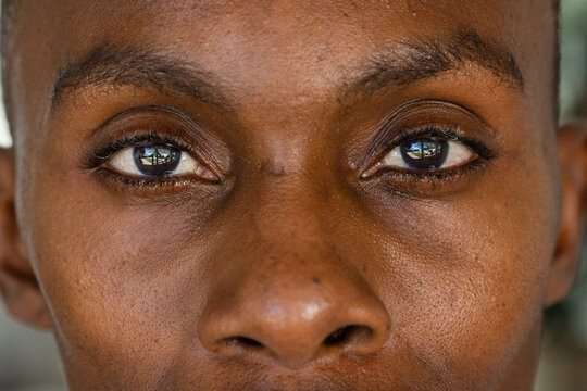Male holding steady gaze toward camera in tight close-up portrait showing window reflection