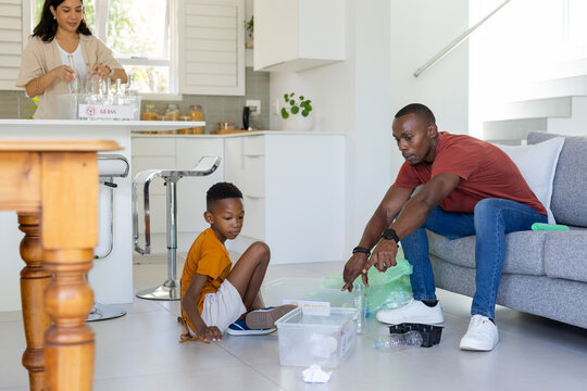 Diverse family sorting recyclables in open-plan kitchen, father placing bottles into clear bin