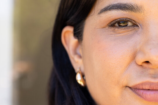 Mid-adult woman gazing, highlighting right eye and gold hoop earring near doorway in warm light