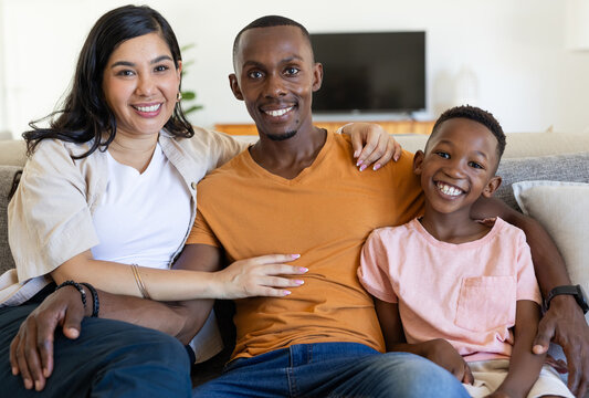 Diverse family sitting on sofa in bright living room, smiling with wristwatch and TV visible