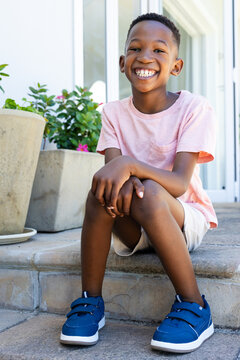 African school-age male child sitting on stoop steps smiling wearing pink shirt beside planters