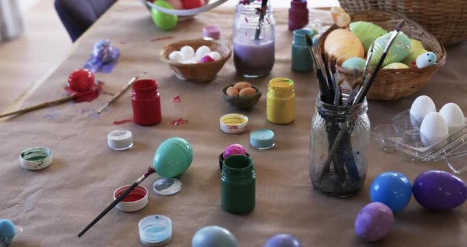 Camera is shifting focus to highlight brush jar, paint jars and pastel eggs on brown paper
