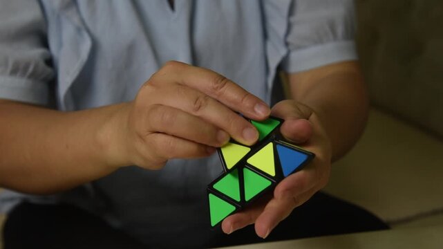 A woman is playing with a triangular Rubik's Cube, close-up shot of her hands.