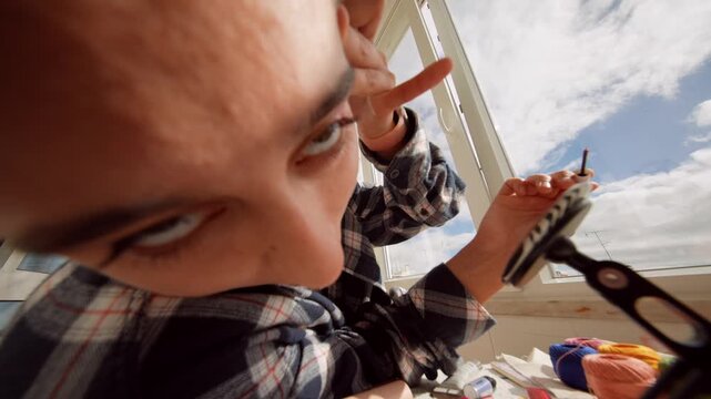 Woman carefully testing eyeliner while leaning on balcony railing