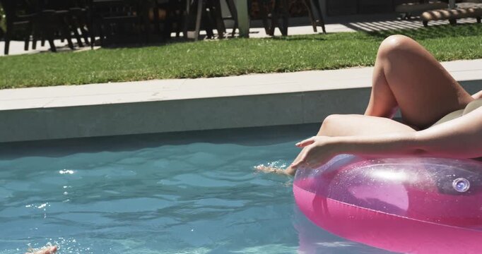 Sunny day inspiring adult woman and youth girl playing on pink floats at pool, cooling off