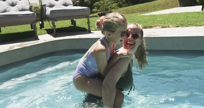 Mom and daughter playing in backyard pool, child climbing onto mom's back, mom bracing in swimsuits