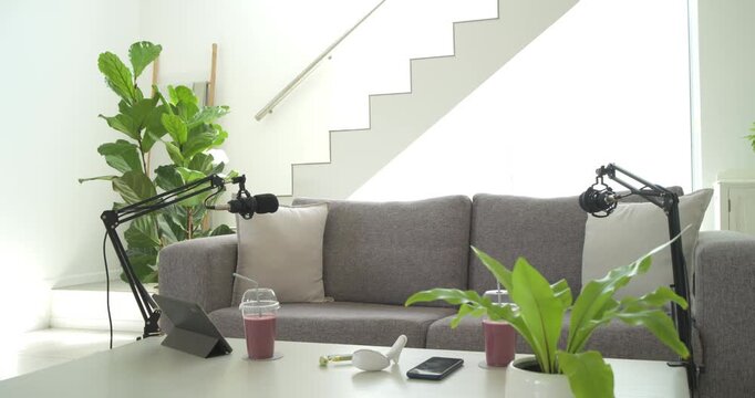 Camera is pulling back to reveal grey sofa and podcast setup as mic arms are adjusting