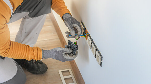 Electrical installation. An electrician's hands during installation a wall sockets to multi pack socket. 