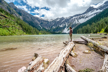 A woman stands on a log in front of a lake © ExploringandLiving