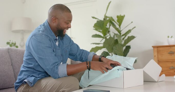 Man sitting on sofa finding white shoe box on coffee table, unwrapping tissue, admiring black shoes