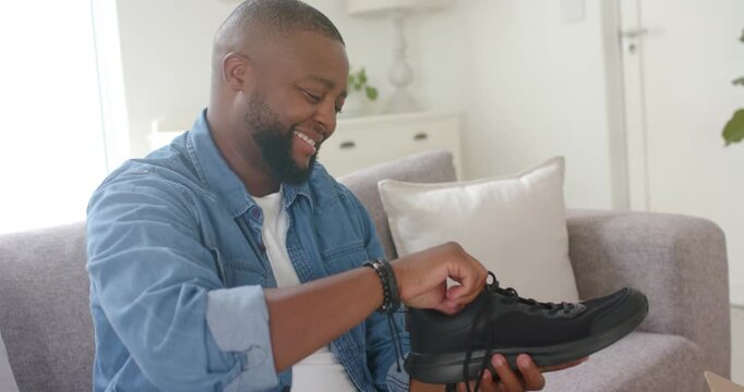 Man sitting on sofa opening shoebox and examining black sneaker, threading laces while checking fit