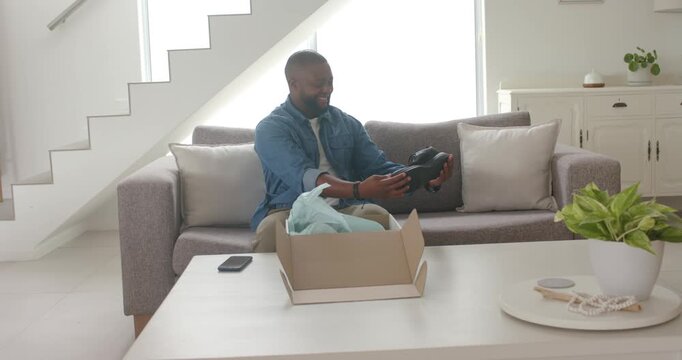 Adult African American male seeing open box on sofa, lifting and checking black shoe quality