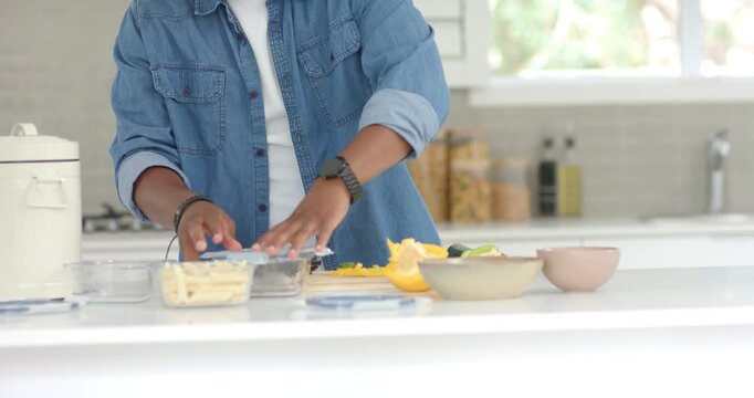 Adult African man packing clear food containers at counter after chopping vegetables, securing lids