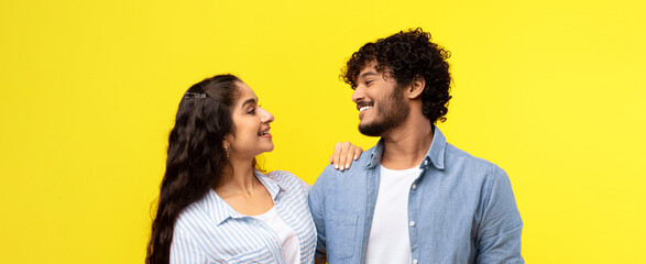 A young couple stands close together with smiles on their faces. They are dressed casually and look happy in front of a bright yellow background. They share a moment of connection and fun. © Prostock-studio