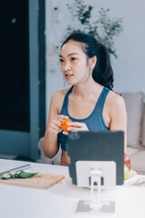 Fit young Asian women in activewear sitting on yoga mat and eating fresh vegetable salad after workout, representing clean eating, fitness lifestyle, wellness routine and health balance.