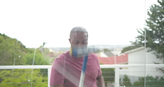 Adult male on balcony by railing spraying glass with sprayer wiping with squeegee removing streaks