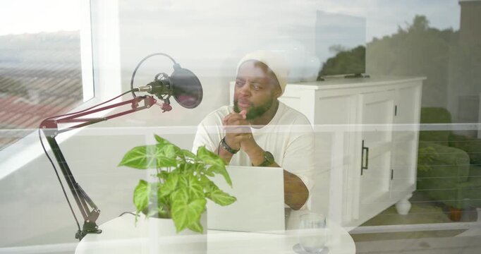 African American man sitting at small round table, recording into boom mic by laptop, sipping water