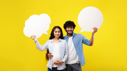 A couple stands together in front of a yellow background. The woman is pregnant and holds a large speech bubble. The man also holds a speech bubble. Both are smiling. © Prostock-studio