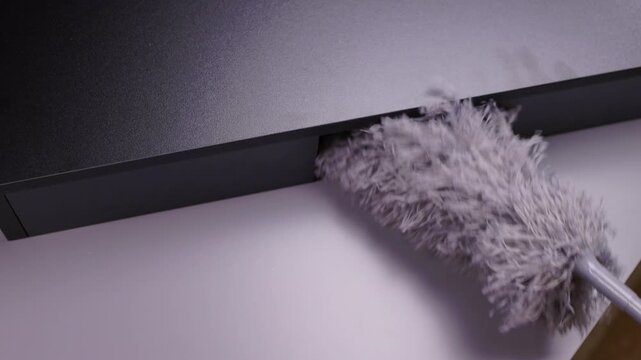 Cleaning wooden furniture after assembly using soft gray microfiber duster removing sawdust and wood chips, maintaining hygiene in dark domestic setting, close-up. Concept of household chores.