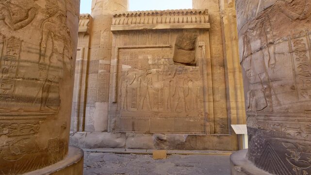 Kom Ombo temple columns with composite capitals and hieroglyphic carvings viewed from below against blue sky in Egypt, upward perspective of ancient sandstone architecture.