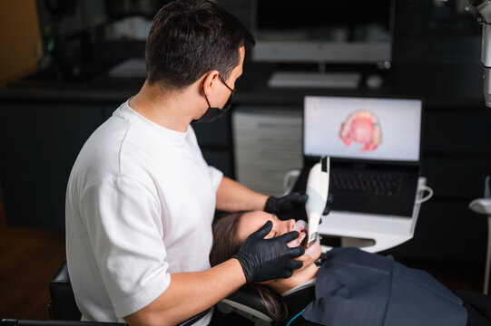 Dentist Examining Patient In Dental Chair With Intraoral Camera And Monitor Displaying Tooth Model, Clinician
