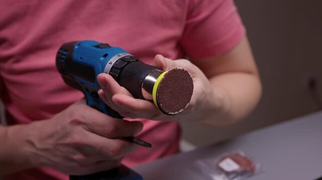 Handyman changing sanding disc attachment to screwdriver bit on cordless power drill, getting ready for woodworking, repair or assembly in workshop environment.